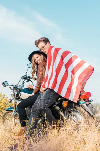 Sonriente pareja con bandera americana sentada en el prado, concepto del día de la independencia - foto de stock