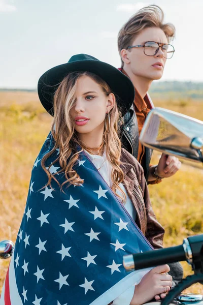 Jovem casal com bandeira americana sentado em moto, conceito de dia de independência — Fotografia de Stock