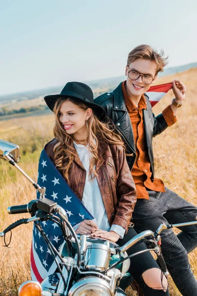 Couple heureux avec drapeau américain assis sur moto vintage, concept de fête de l'indépendance — Photo de stock