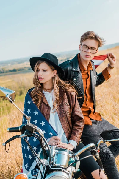 Jeune couple avec drapeau américain assis sur moto, concept de fête de l'indépendance — Photo de stock