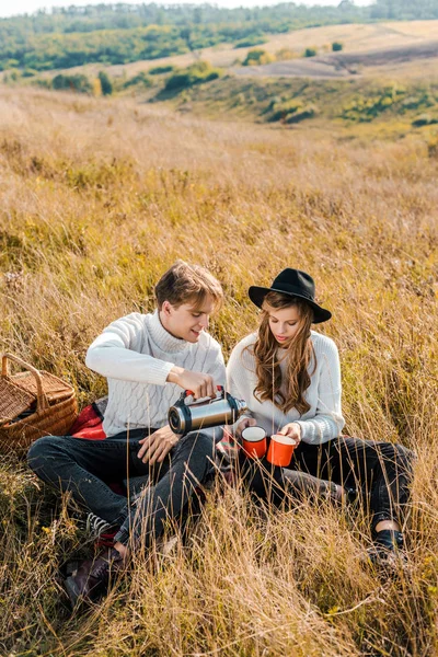 Young couple pouring tea from thermos on rural meadow — Stock Photo