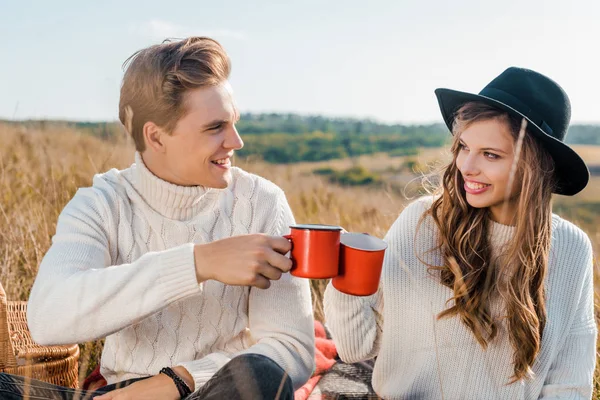 Happy couple clinking with orange cups on rural meadow — Stock Photo