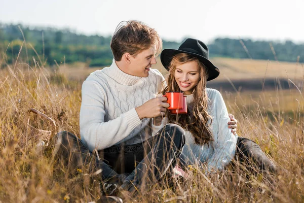 Glückliches junges Paar mit Tassen entspannt auf bäuerlicher Wiese — Stockfoto