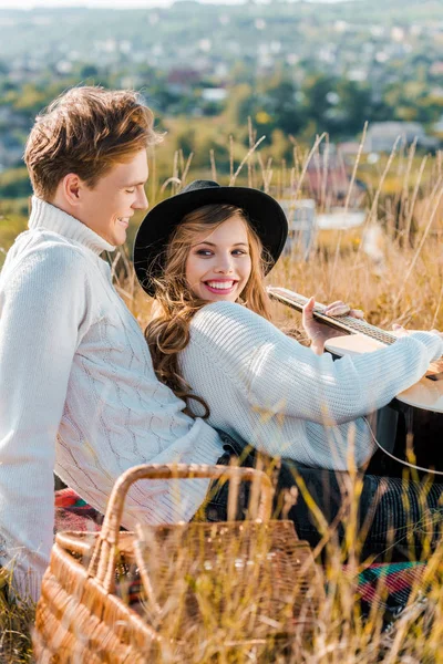 Sonriente novia sosteniendo la guitarra mientras novio relajarse en la hierba - foto de stock