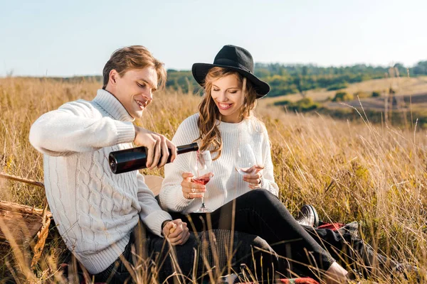 Novio joven verter vino tinto para la novia durante el picnic en el prado - foto de stock