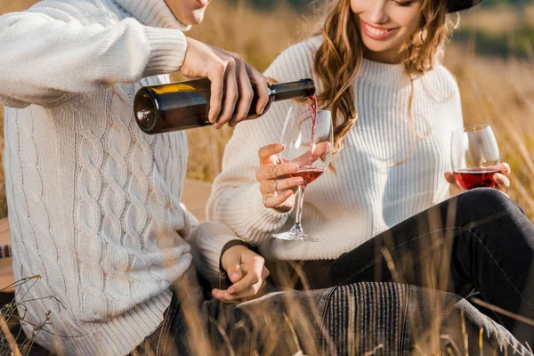 Cropped view of couple pouring red wine on meadow — Stock Photo