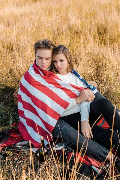 Pareja joven con bandera americana descansando sobre cuadros, concepto del día de la independencia - foto de stock