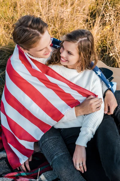 Sonriente pareja con bandera americana en el picnic, concepto del día de la independencia - foto de stock