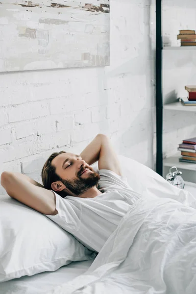 Улыбающийся молодой бородатый мужчина просыпается в спальне дома — стоковое фото