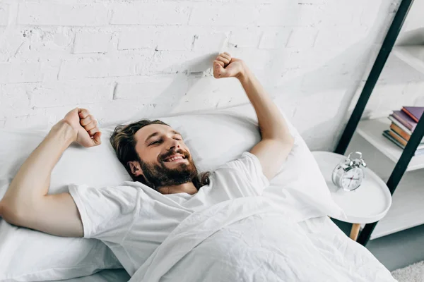Hombre barbudo feliz haciendo estiramiento en la cama durante la mañana en casa - foto de stock