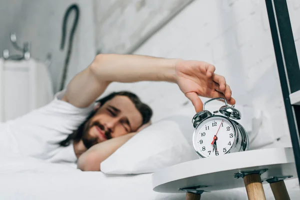 Enfoque selectivo de Jesús molesto apagar el despertador durante la mañana en el dormitorio en casa — Stock Photo