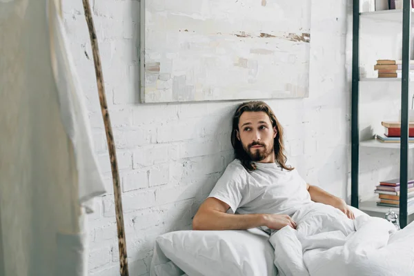 Selective focus of Jesus waking up in bed and looking at own robe and wooden staff at home — Stock Photo