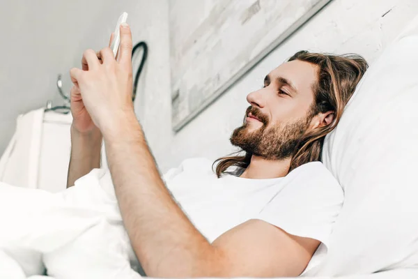 Happy Jesus using smartphone in bed during morning time at home — Stock Photo