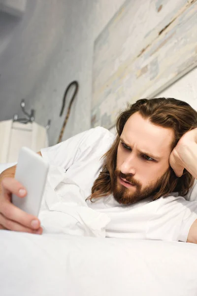 Focalizzato Gesù utilizzando lo smartphone a letto durante il mattino a casa — Foto stock