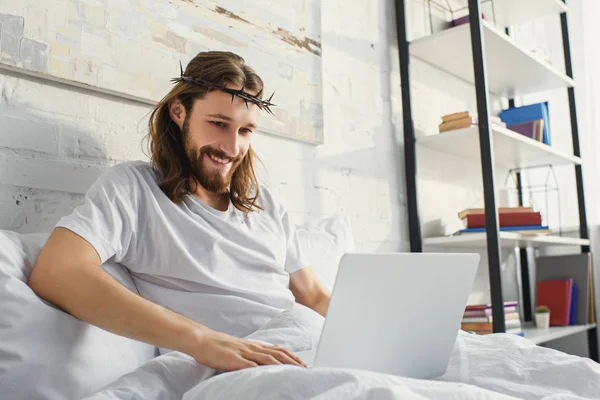Счастливый Иисус, используя ноутбук в постели в утреннее время дома — стоковое фото