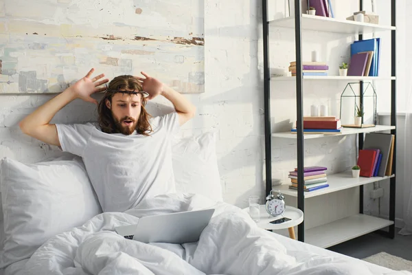 Shocked Jesus gesturing by hands in bed with laptop during morning time at home — Stock Photo