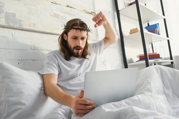 Jesús emocional usando el ordenador portátil y el gesto a mano en la cama durante el tiempo de la mañana en casa - foto de stock