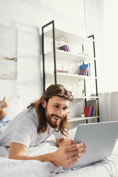 Smiling Jesus using laptop in bed during morning time at home — Stock Photo
