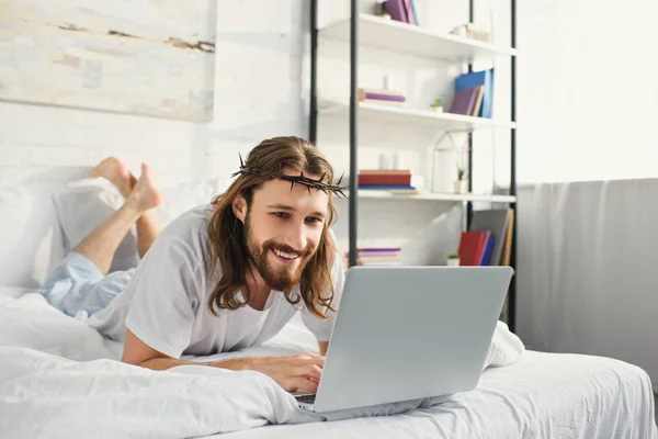 Lächelnder Jesus mit Laptop im Bett am Morgen zu Hause — Stockfoto