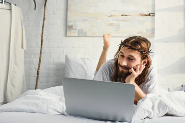 Feliz Jesús usando el ordenador portátil en la cama durante la mañana en casa - foto de stock
