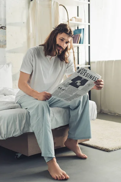 Улыбаясь, Иисус в терновом венце читает деловую газету в спальне в утреннее время дома — стоковое фото