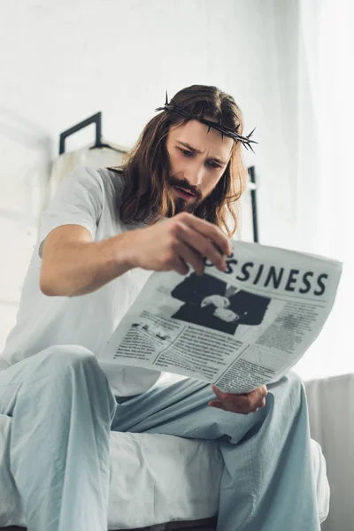 Low angle view of Jesus in crown of thorns reading business newspaper in bedroom during morning time at home — Stock Photo