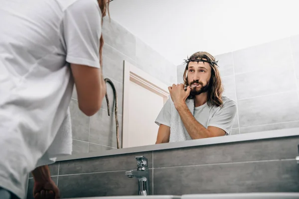 Vue partielle de Jésus avec serviette sur les épaules se brossant les dents et regardant son propre reflet dans la salle de bain — Photo de stock