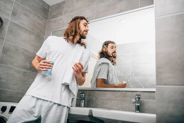 Visão de baixo ângulo de Jesus na coroa de espinhos enxaguando a boca por líquido de enxaguamento bucal no banheiro — Fotografia de Stock