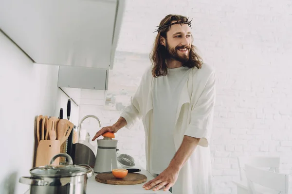 Счастливый Иисус смотрит в сторону и делает апельсиновый сок соком на кухне дома — стоковое фото