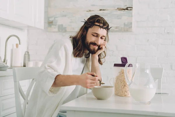 Улыбаясь Иисус ест кукурузные хлопья на завтрак на кухне дома — стоковое фото