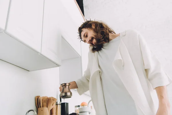 Низкий угол зрения Иисуса, говорящего по смартфону и варищего кофе с цезве на кухне в утреннее время дома — стоковое фото