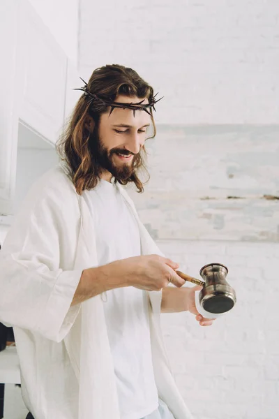Улыбающийся Иисус наливает кофе из cezve в чашку на кухне в утреннее время дома — стоковое фото