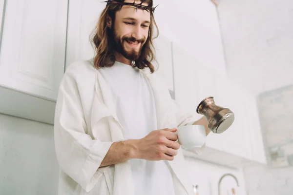 Low angle view of happy Jesus pouring coffee from cezve into cup in kitchen during morning time at home — Stock Photo