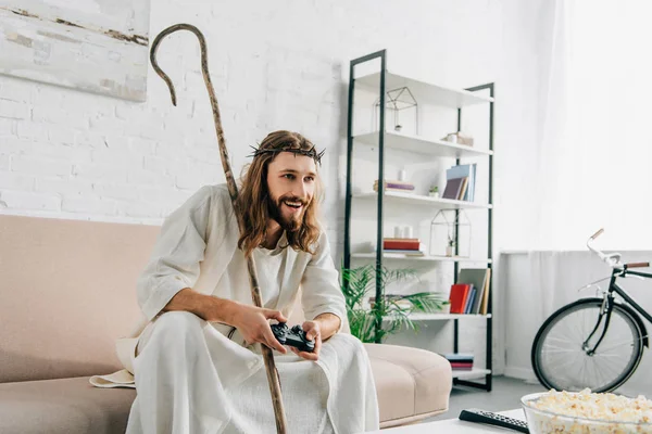 Jesus feliz com a equipe de madeira jogando videogame por joystick no sofá em casa — Fotografia de Stock