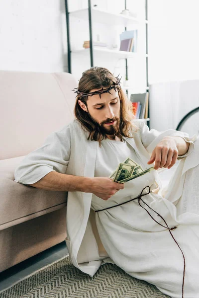 Selektiver Fokus von Jesus, der auf dem Boden in der Nähe des Sofas sitzt und zu Hause Bargeld zählt — Stockfoto