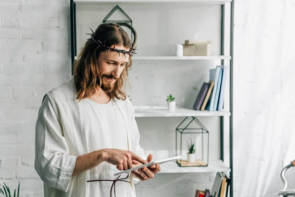 Enfoque selectivo de Jesús en corona de espinas y túnica usando tableta digital en casa - foto de stock