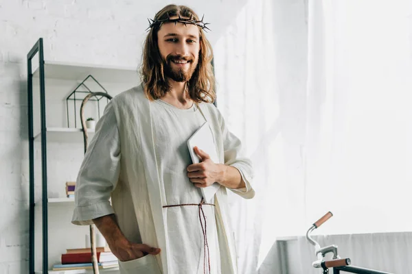 Porträt eines glücklichen Jesus in Dornenkrone, der in die Kamera blickt und das digitale Tablet zu Hause hält — Stockfoto