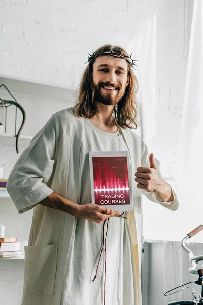 Happy Jesus in crown of thorns doing thumb gesture and showing digital tablet with trading courses at home — Stock Photo