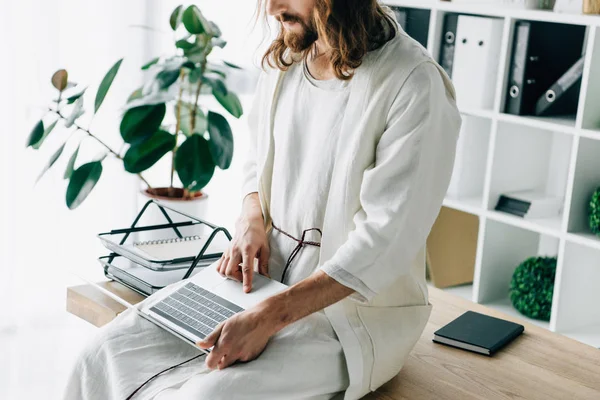 Partial view of Jesus sitting on table and working on laptop in modern office — Stock Photo