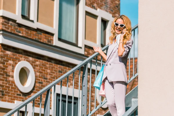 Jeune femme à la mode avec des sacs en papier parlant par téléphone sur les escaliers — Photo de stock