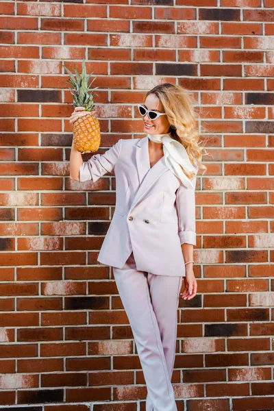 Jeune femme élégante avec ananas debout devant le mur de briques — Photo de stock