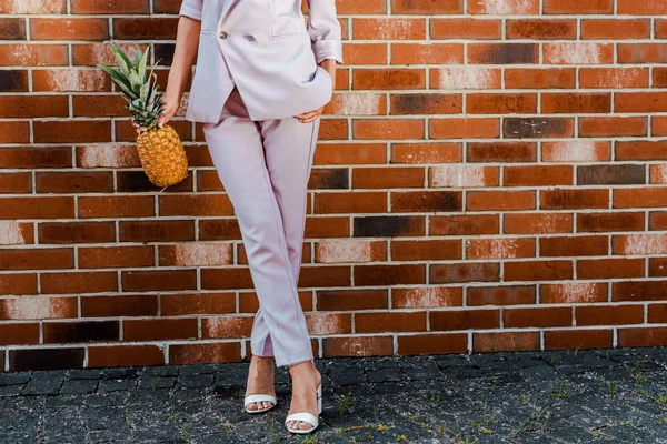 Cropped shot of stylish woman with pineapple standing in front of brick wall — Stock Photo