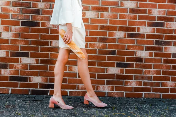 Tiro cortado de mulher elegante segurando baguete na frente da parede de tijolo — Fotografia de Stock