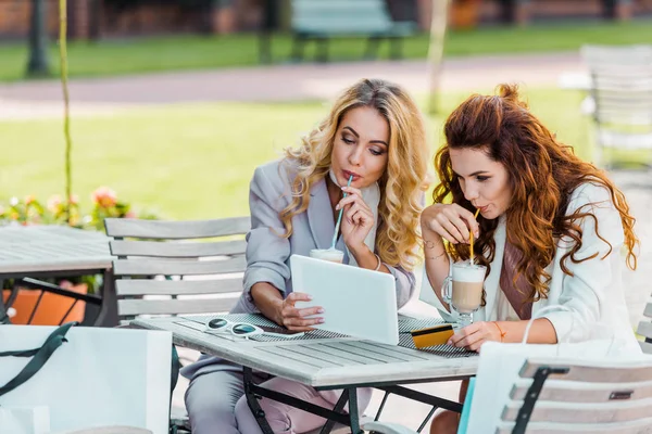 Mujeres jóvenes con estilo con tarjeta de crédito y tableta haciendo e-shopping sentado en la cafetería - foto de stock