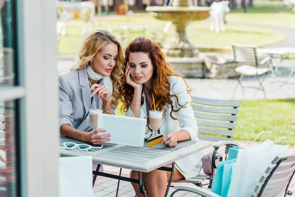 Fashionable young women with credit card and tablet making e-shopping sitting in cafe — Stock Photo