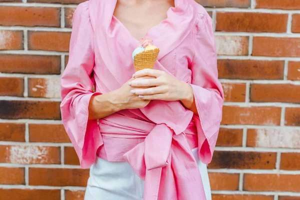 Cropped shot of woman in pink holding ice cream in front of brick wall — Stock Photo