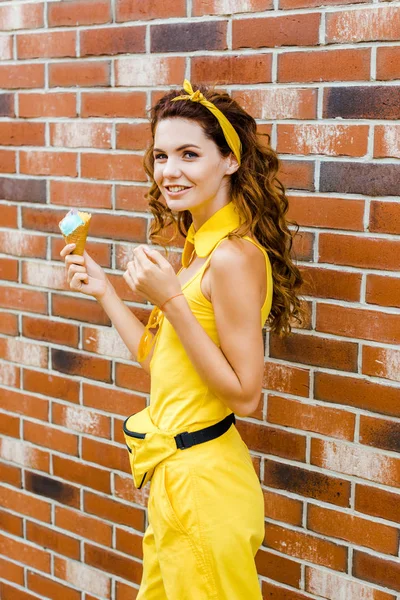 Attraktive junge Frau in gelben Kleidern mit Eis blickt vor Backsteinmauer in die Kamera — Stockfoto