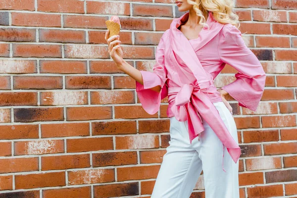 Cropped shot of young woman in pink holding ice cream in front of brick wall — Stock Photo