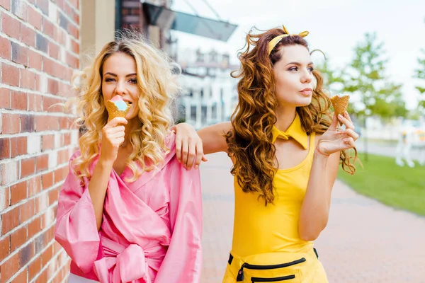 Fashionable young women in colorful clothes eating ice cream on street — Stock Photo