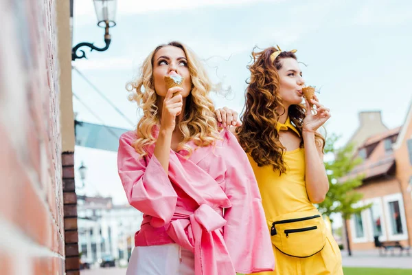 Attractive young women in colorful clothes eating ice cream on street — Stock Photo